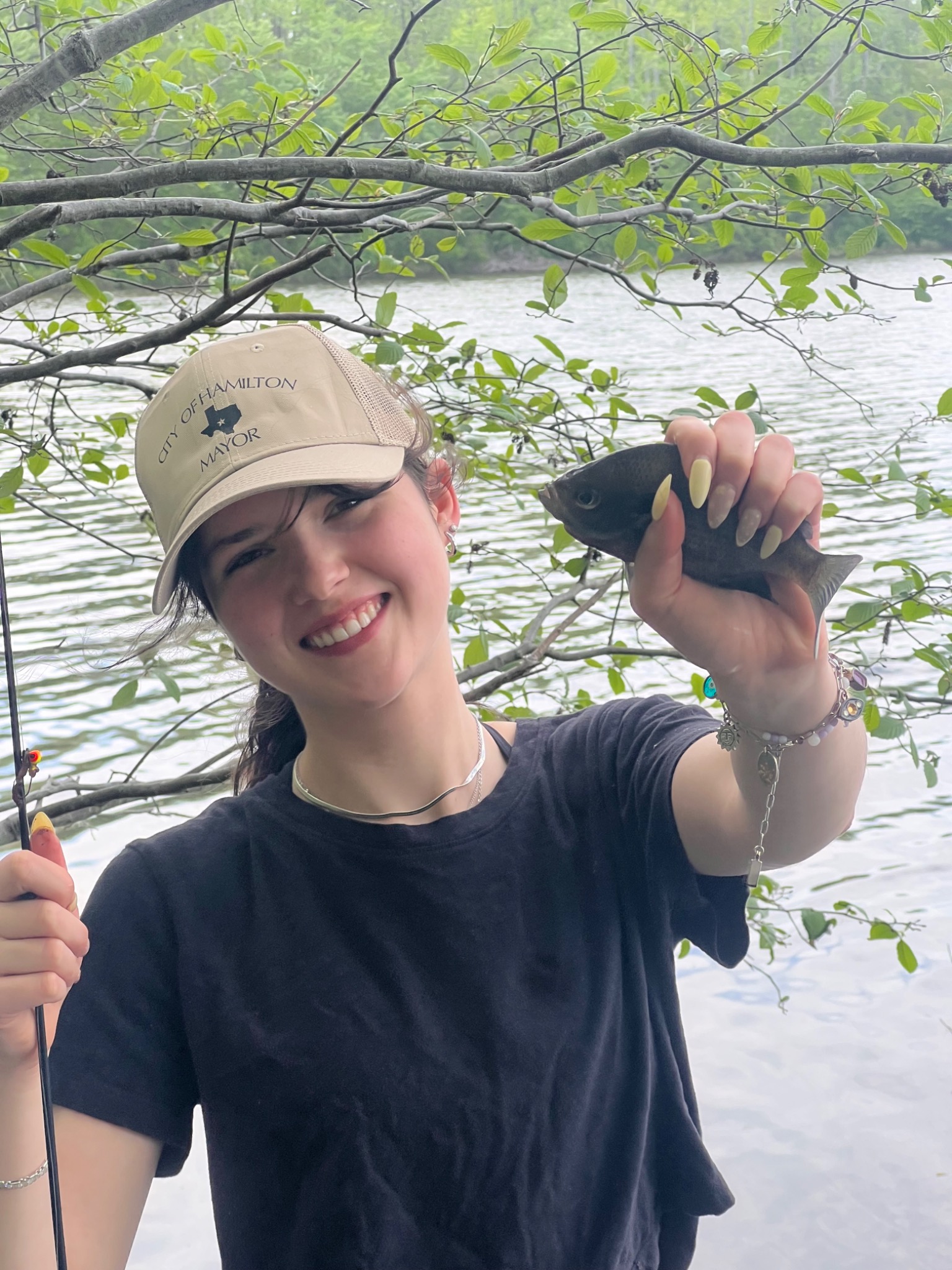 Annabelle smiling beside the water and holding up her catch